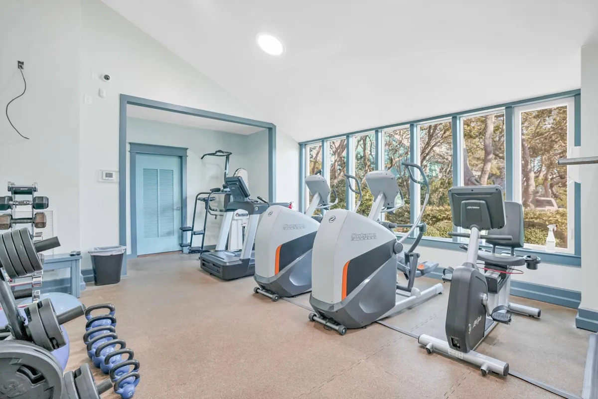 A well-equipped fitness center featuring elliptical machines, stationary bikes, and free weights. The room is bright and modern, creating an energetic atmosphere for individual workouts or group fitness classes. Large windows provide natural light and a view outside, further enhancing the resort feel.