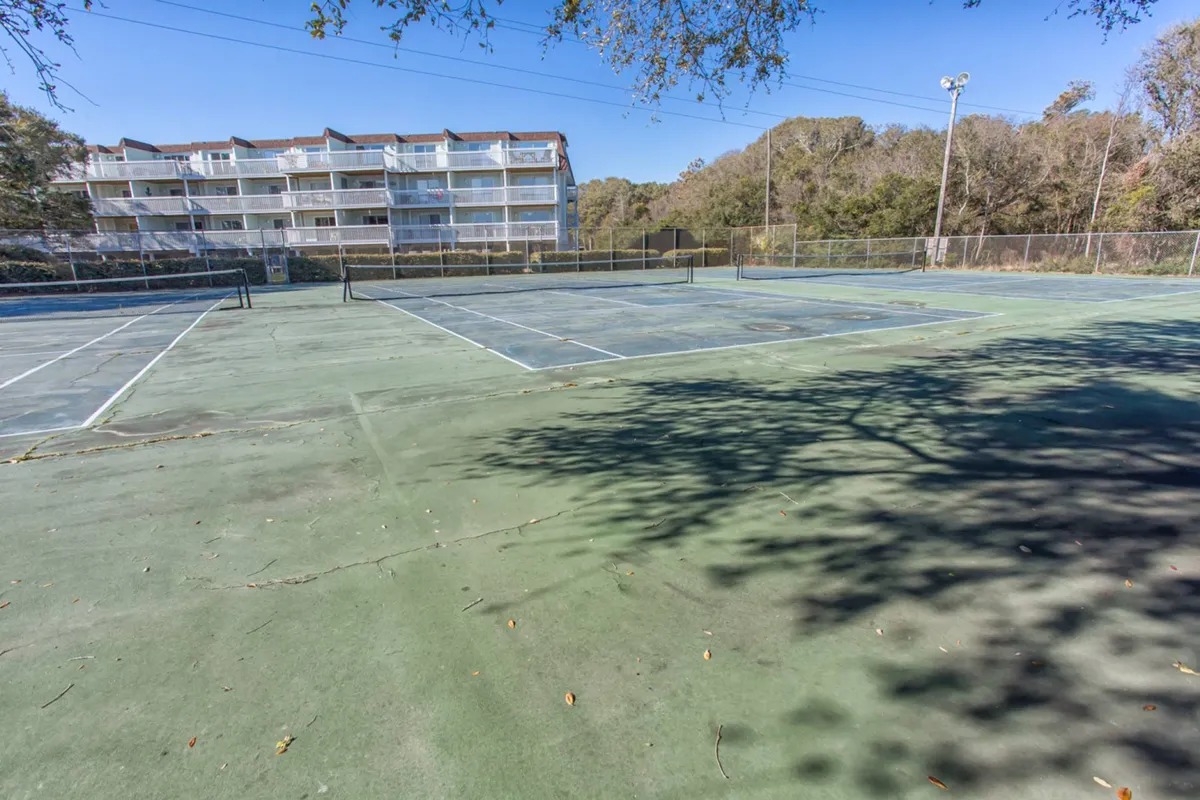 A lively exterior scene of tennis courts surrounded by greenery, with people playing and apartment buildings in the background. The atmosphere is energetic, suggesting friendly matches, community events, and opportunities for outdoor sports.